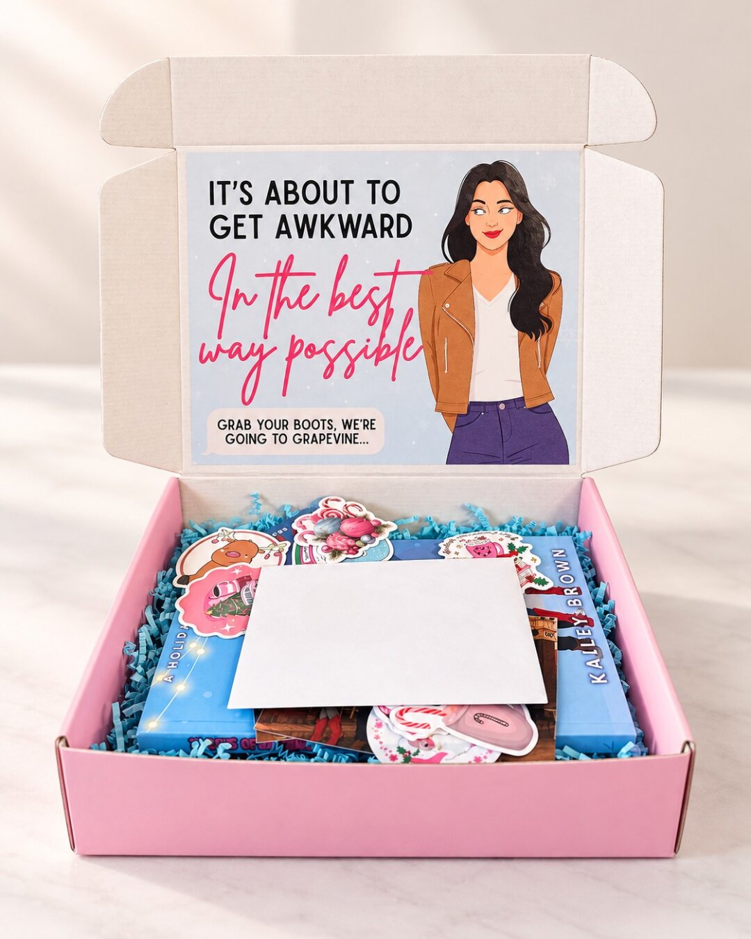 The Awkward Box, open to show a copy of 12 Days of Awkward, character art, stickers and a sealed envelope, under a lid that reads It's about to get awkward, in the best way possible